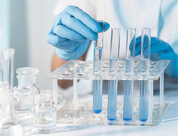 Gloved hands handling test tubes and beakers in a lab